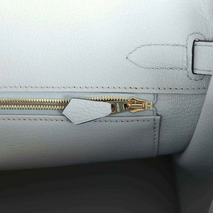 Pale blue leather handbag close-up of gold zipper pull and small tab near stitching