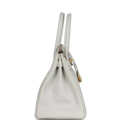 Light gray leather handbag profile view with double top handles and gold accents