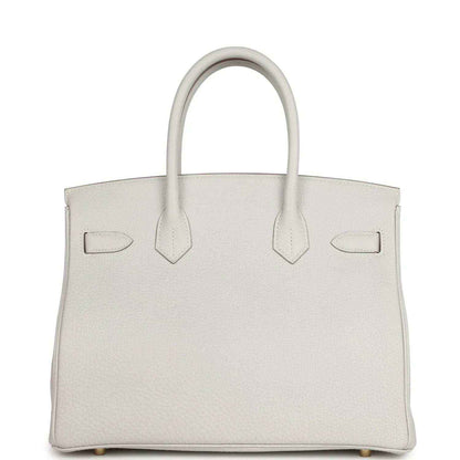 Light gray leather handbag front view with three panel straps, top handles, gold-toned details