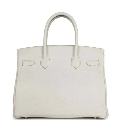 Light gray leather handbag front view with three panel straps, top handles, gold-toned details