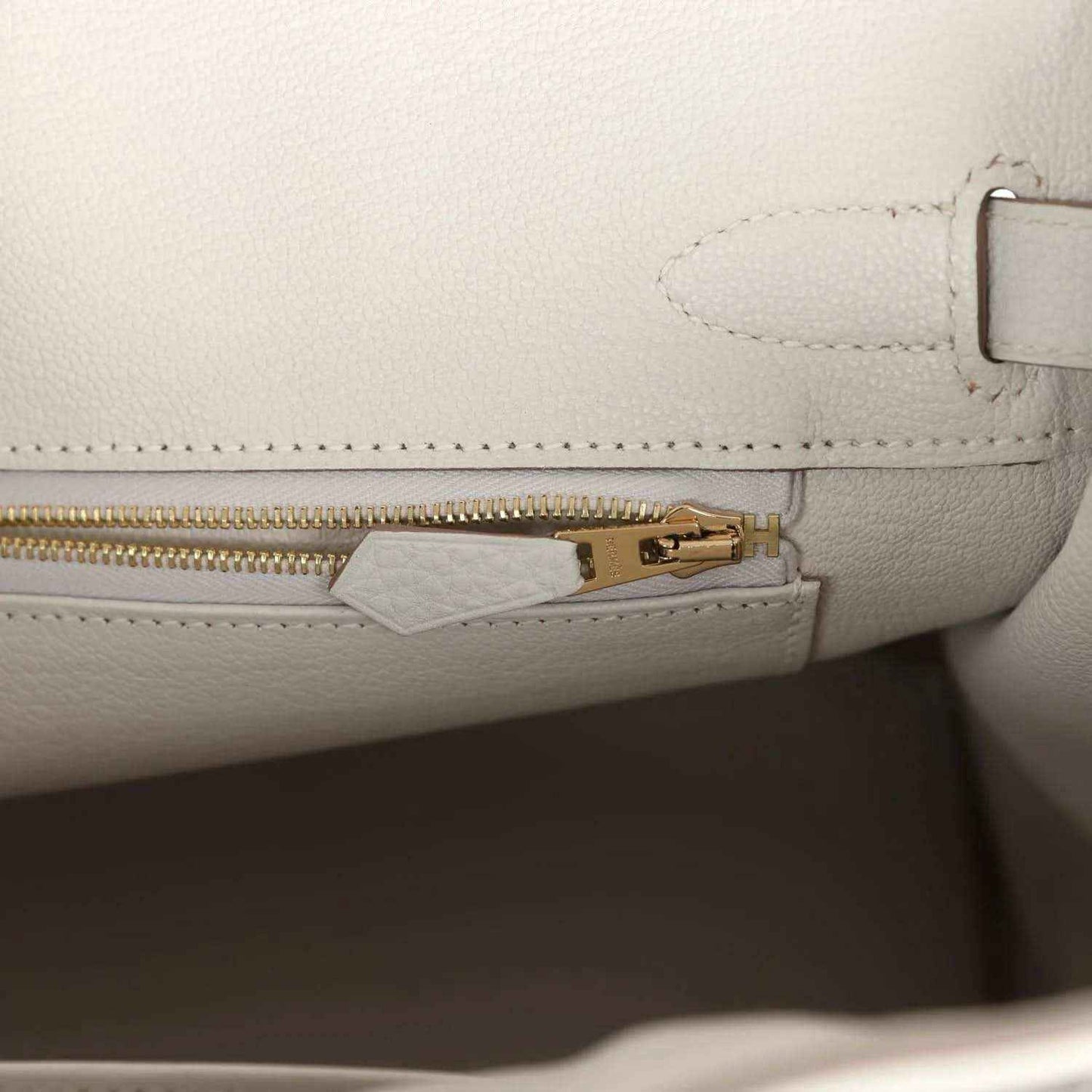 Light gray leather handbag with gold zipper pull and inside tab hardware