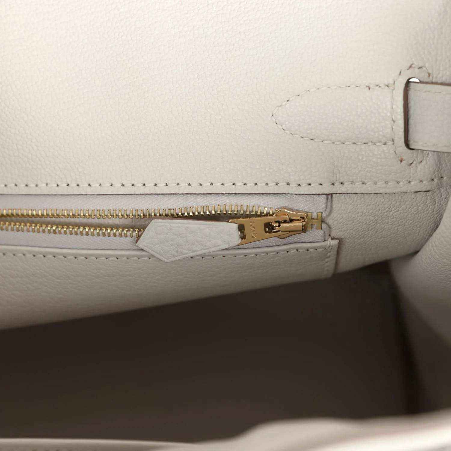 Light gray leather handbag with gold zipper pull and inside tab hardware