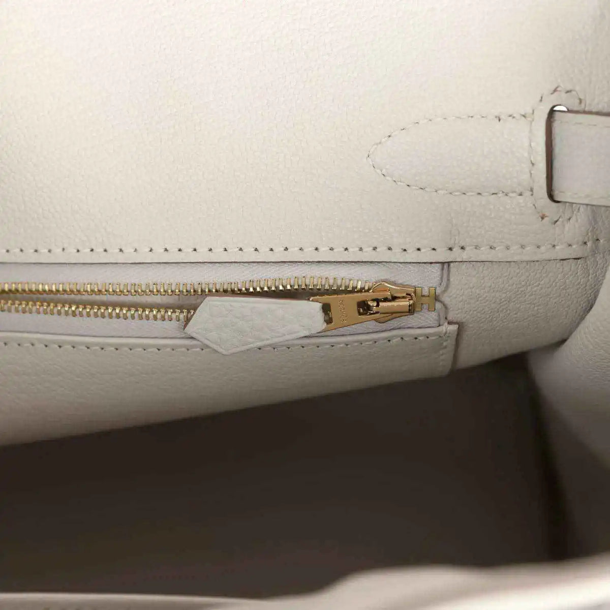 Light gray leather handbag with gold zipper pull and inside tab hardware