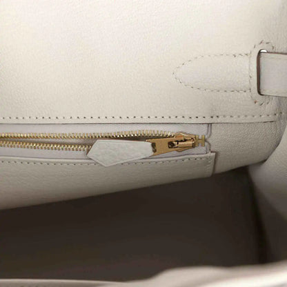 Light gray leather handbag with gold zipper pull and inside tab hardware