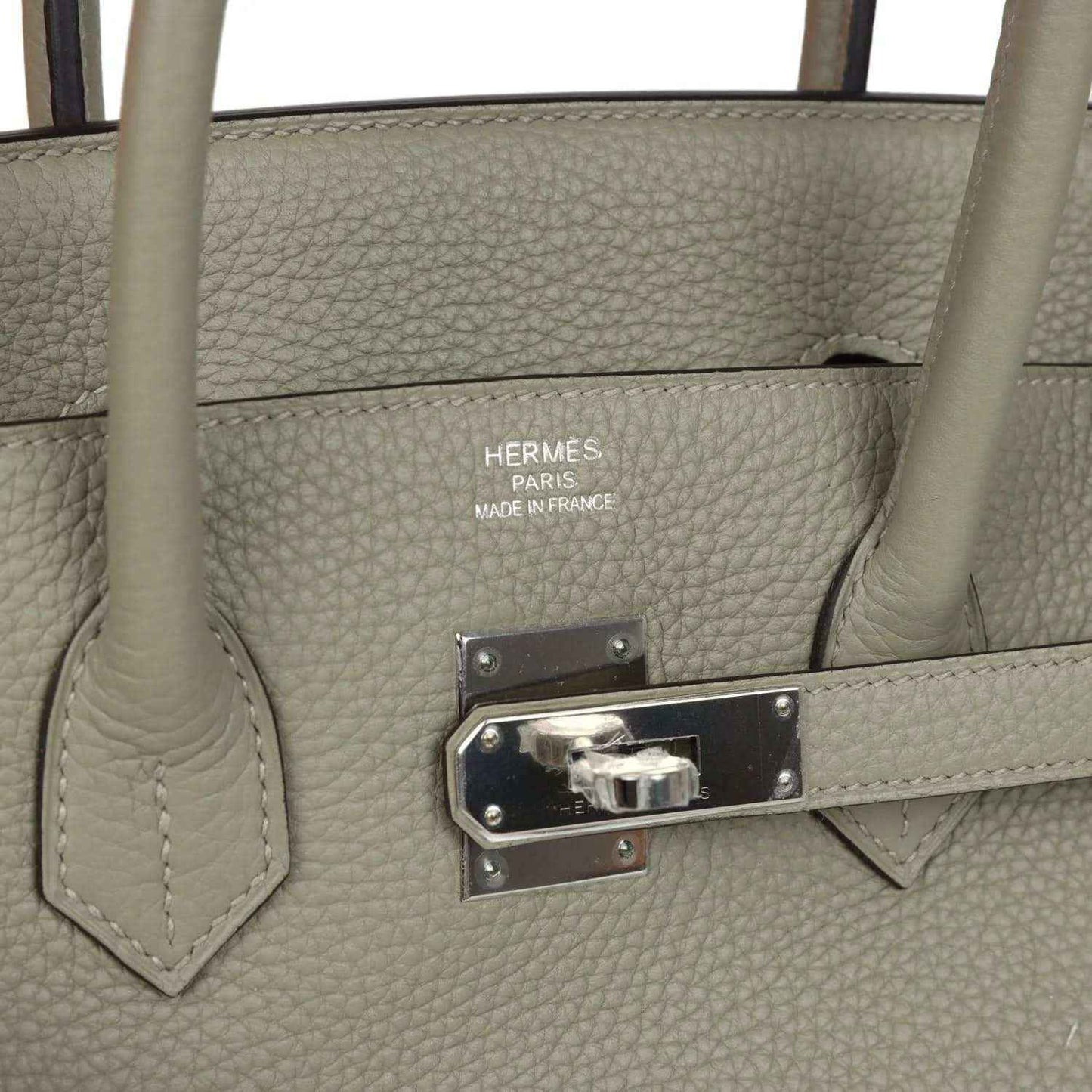 Hermes leather handbag detail with logo, metal clasp plate, and snap hardware