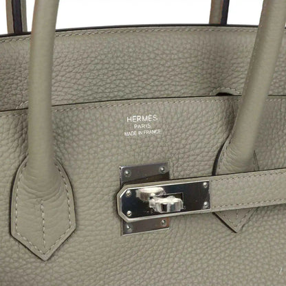 Hermes leather handbag detail with logo, metal clasp plate, and snap hardware