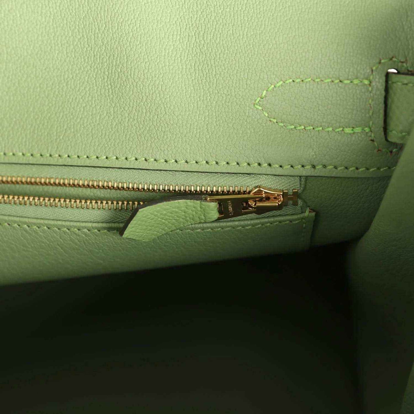 Green leather handbag with gold-tone zipper pull and stitched pocket edge