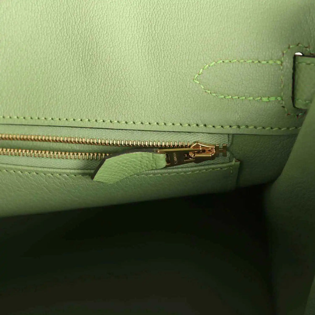Green leather handbag with gold-tone zipper pull and stitched pocket edge