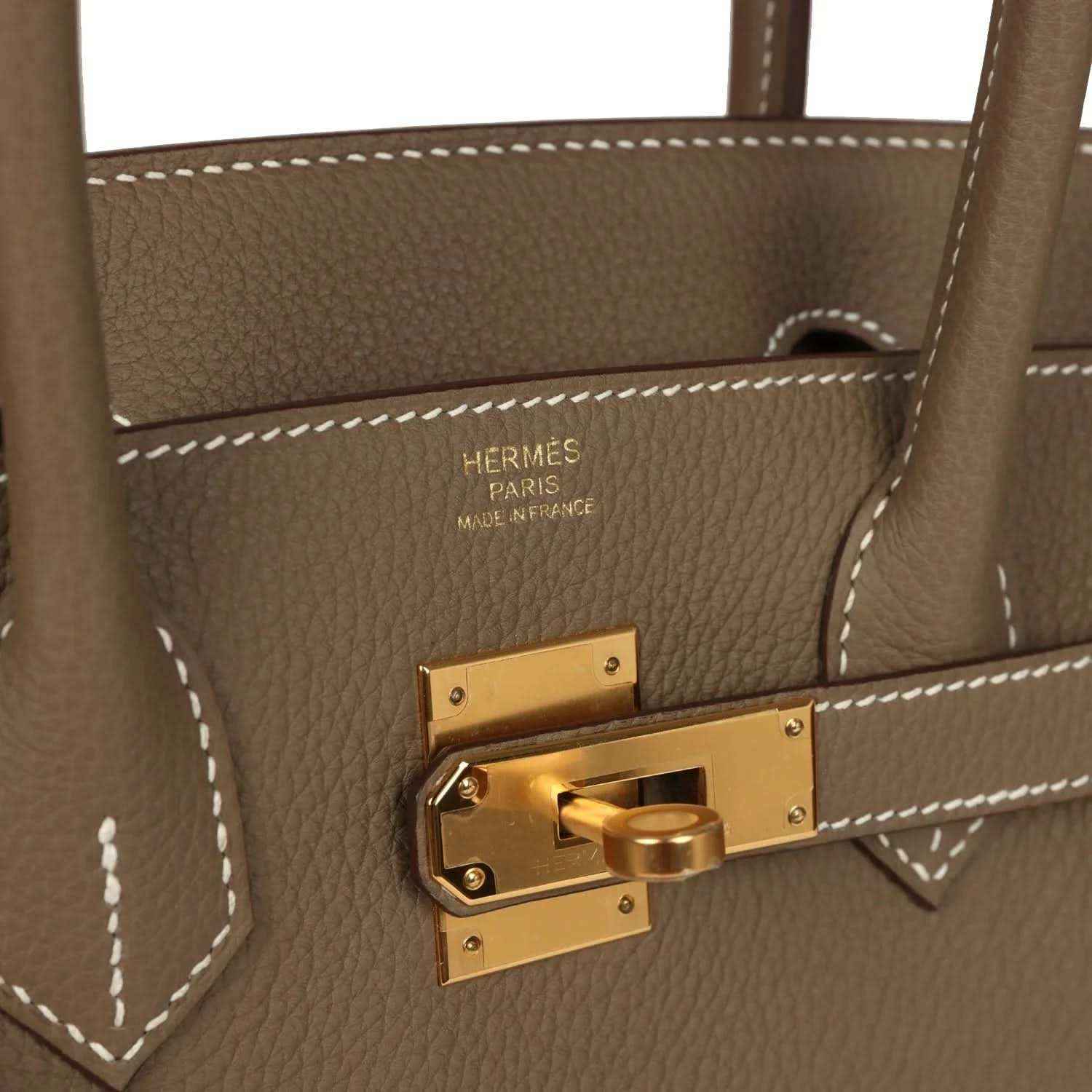 Hermes Birkin lock plate in gold tone with engraved 'Hermes Paris' on taupe leather.