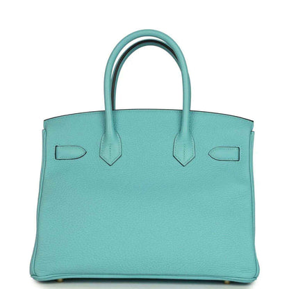 Teal leather handbag with structured sides, top handles, and gold-tone base feet