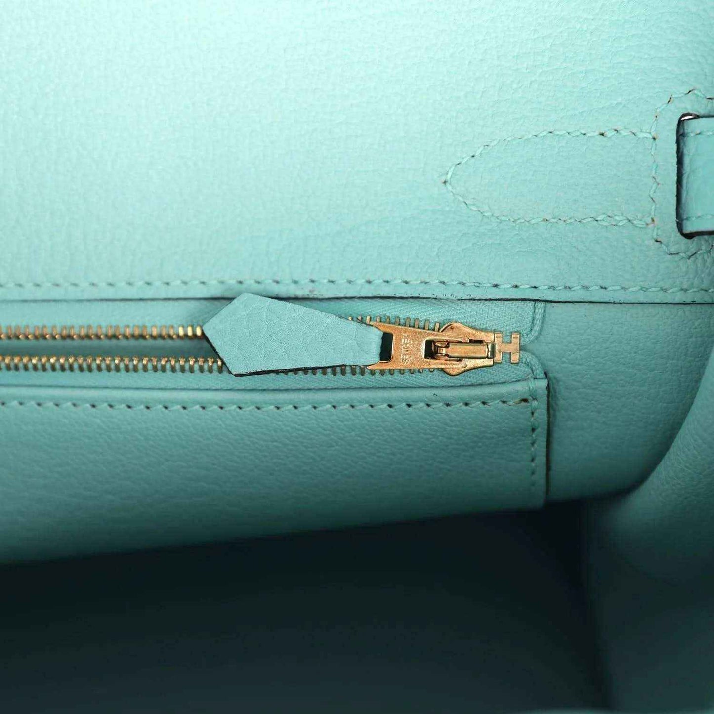 Close-up of teal leather handbag zipper edge and gold-tone hardware with H emblem