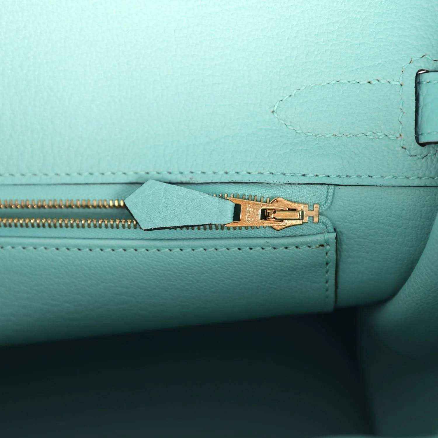 Close-up of teal leather handbag zipper edge and gold-tone hardware with H emblem
