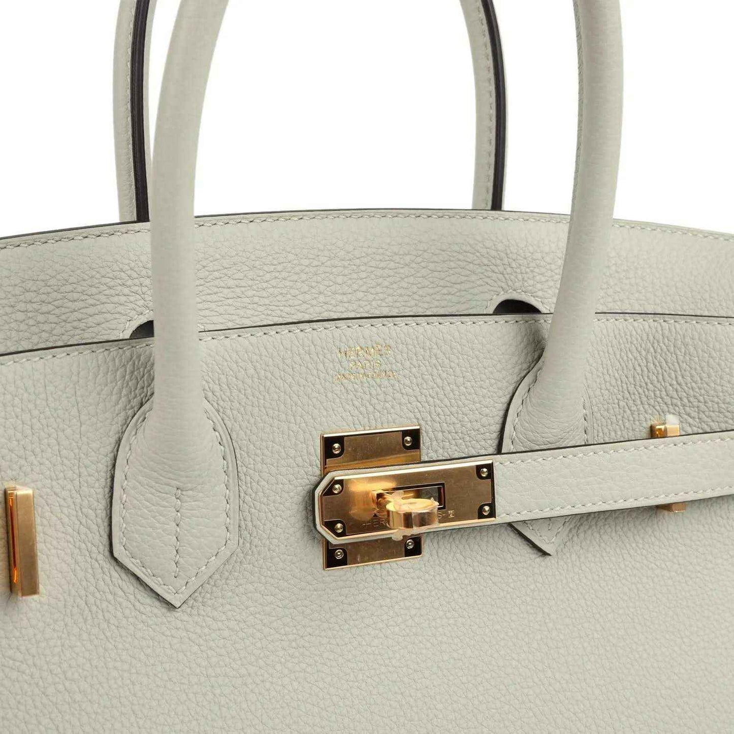 Light gray leather handbag front with gold-toned lock hardware and top handle attachments