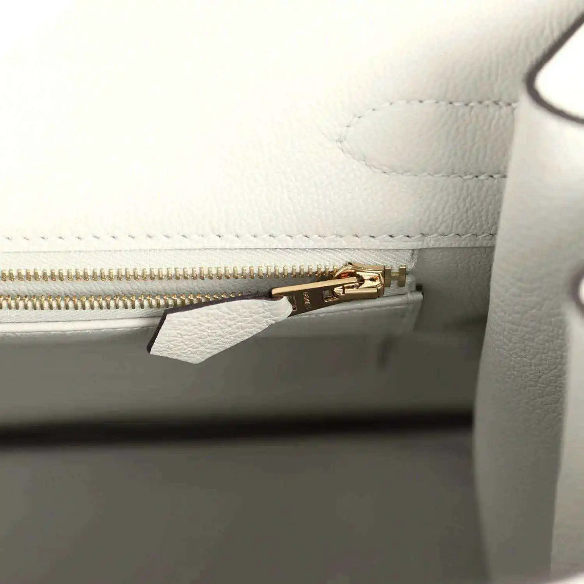 Light gray leather handbag interior with gold zipper and small hardware clip