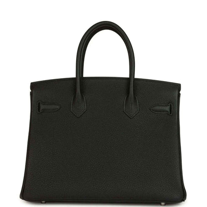 Black leather handbag front with top handles, stitched seams and flap pocket detailing.