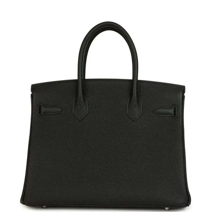 Black leather handbag front with top handles, stitched seams and flap pocket detailing.