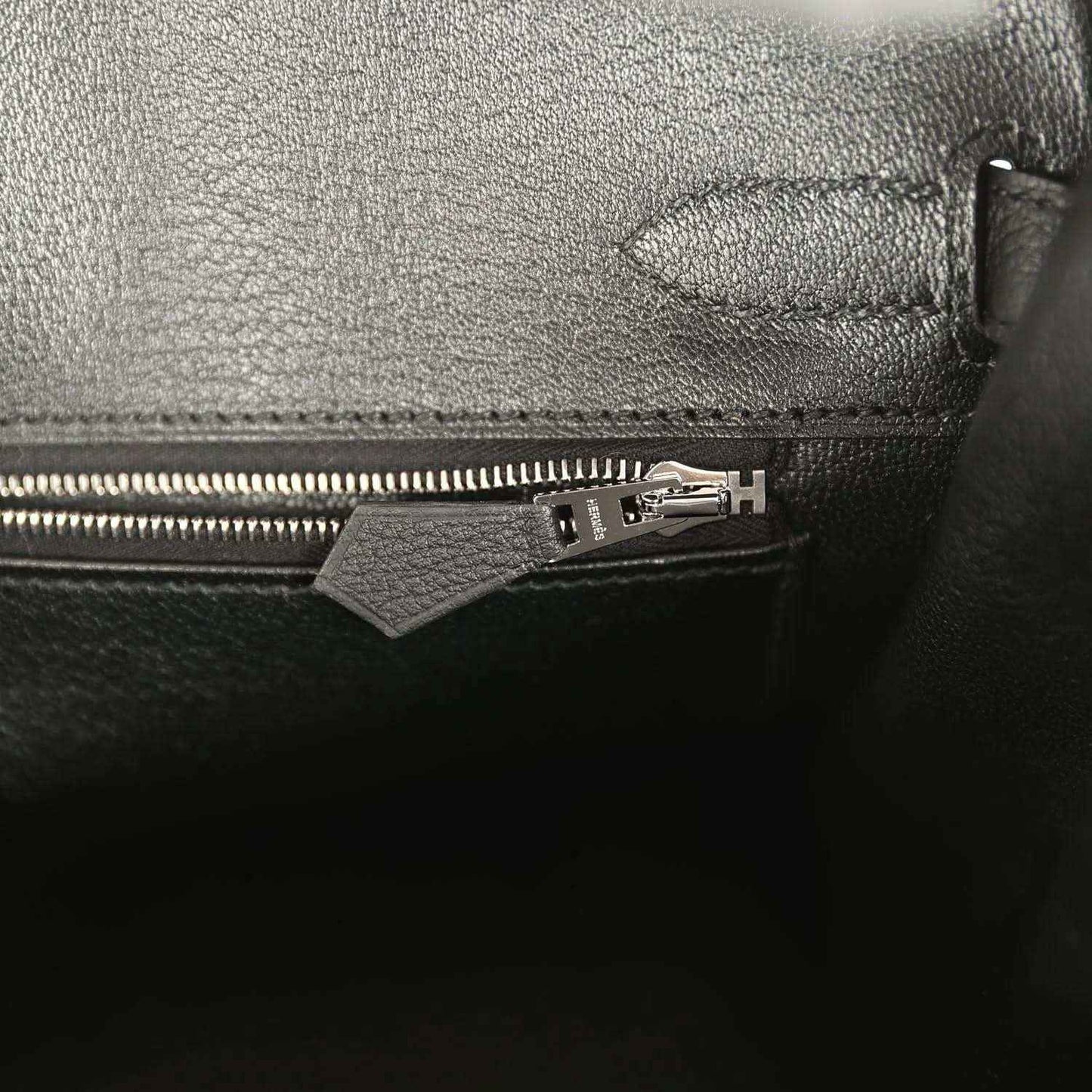 Black leather handbag pocket with zipper pull and metal hardware.