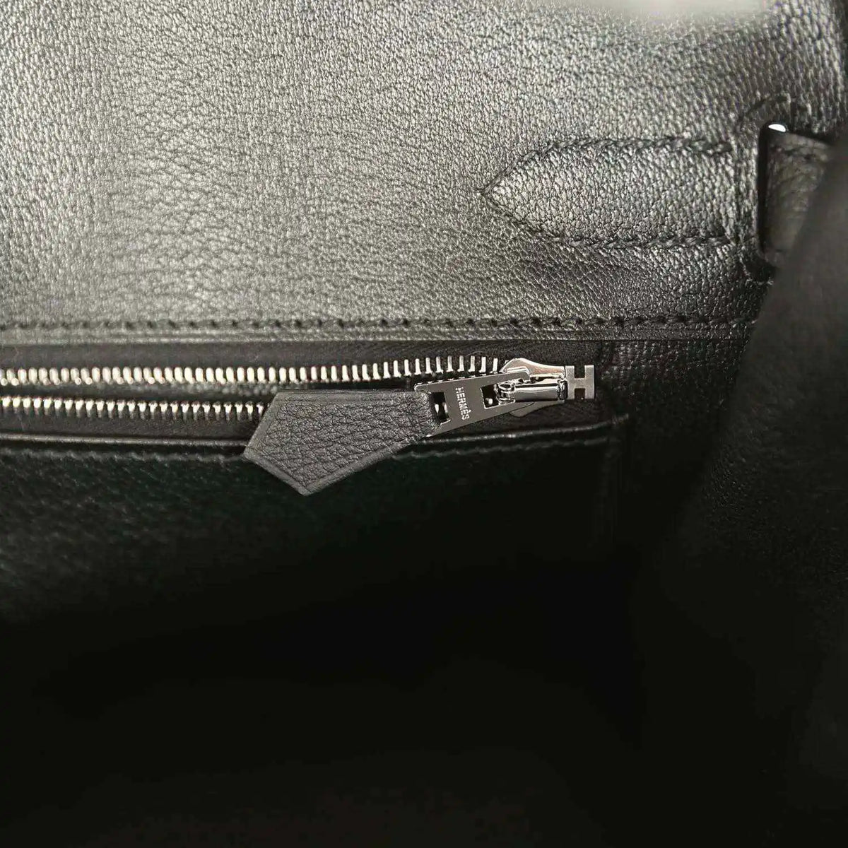 Black leather handbag pocket with zipper pull and metal hardware.