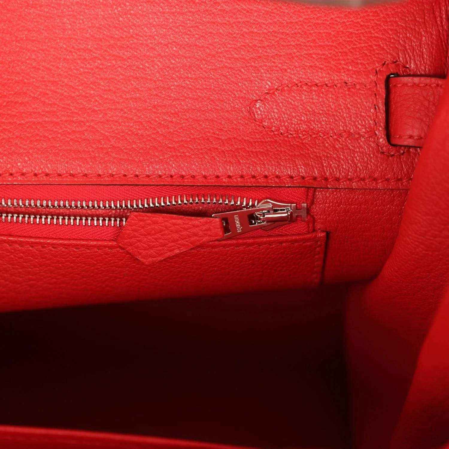 Red Birkin bag interior pocket with metal zipper and stitched leather trim.