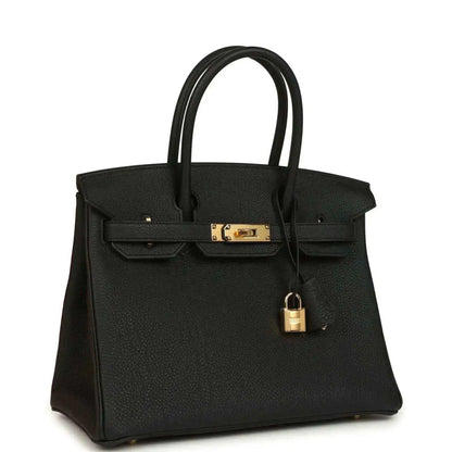 Black leather handbag with top handles, front flap, and gold lock hardware