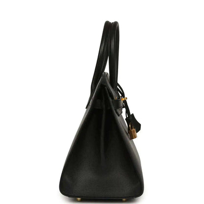 Black leather handbag side view with top handles and gold base feet