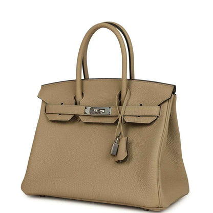 Tan leather handbag with top handles, front flap, and hanging lock charm