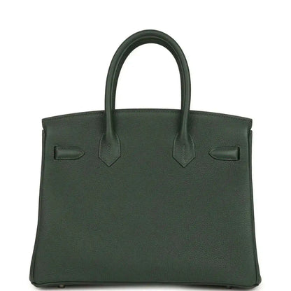 Green leather handbag with top handles and front flap details; decorative corner tabs