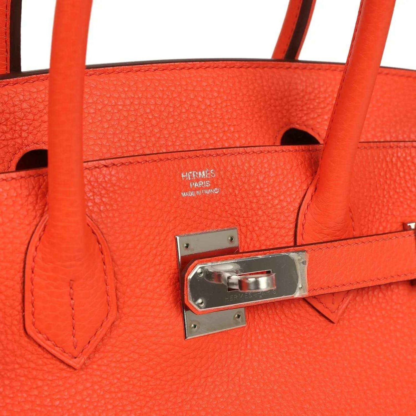 Orange handbag close-up with embossed logo, turnlock plate, and stitched leather trim