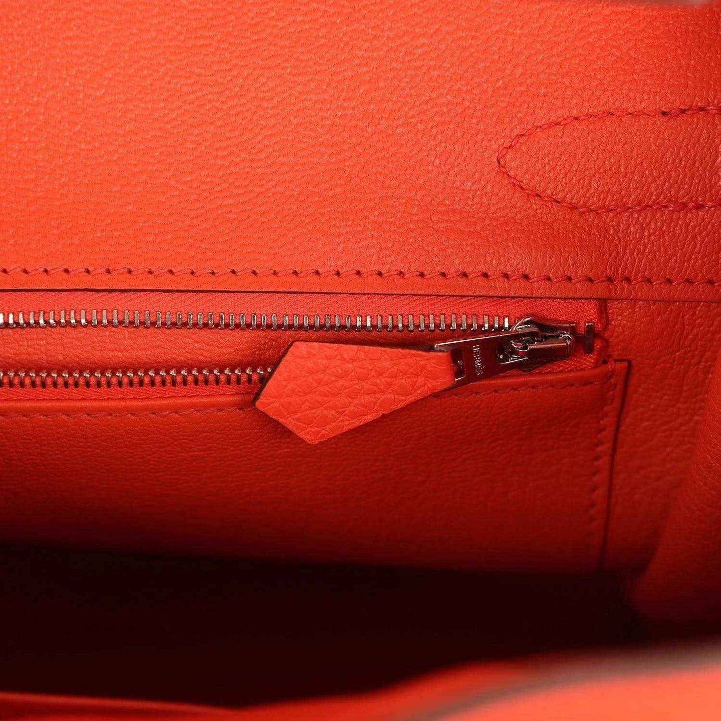 Orange handbag close-up of zipper and leather pocket with stitched edging and hardware
