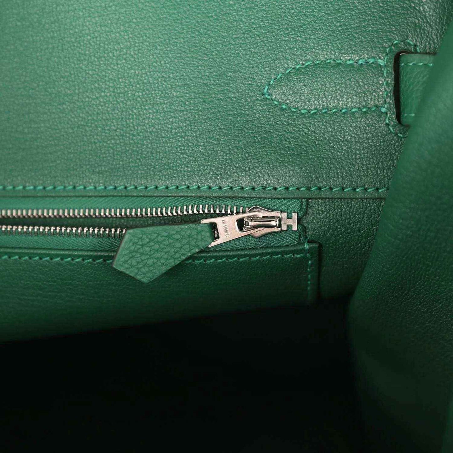 Green leather handbag interior detail with silver zipper pull and stitched seam trim