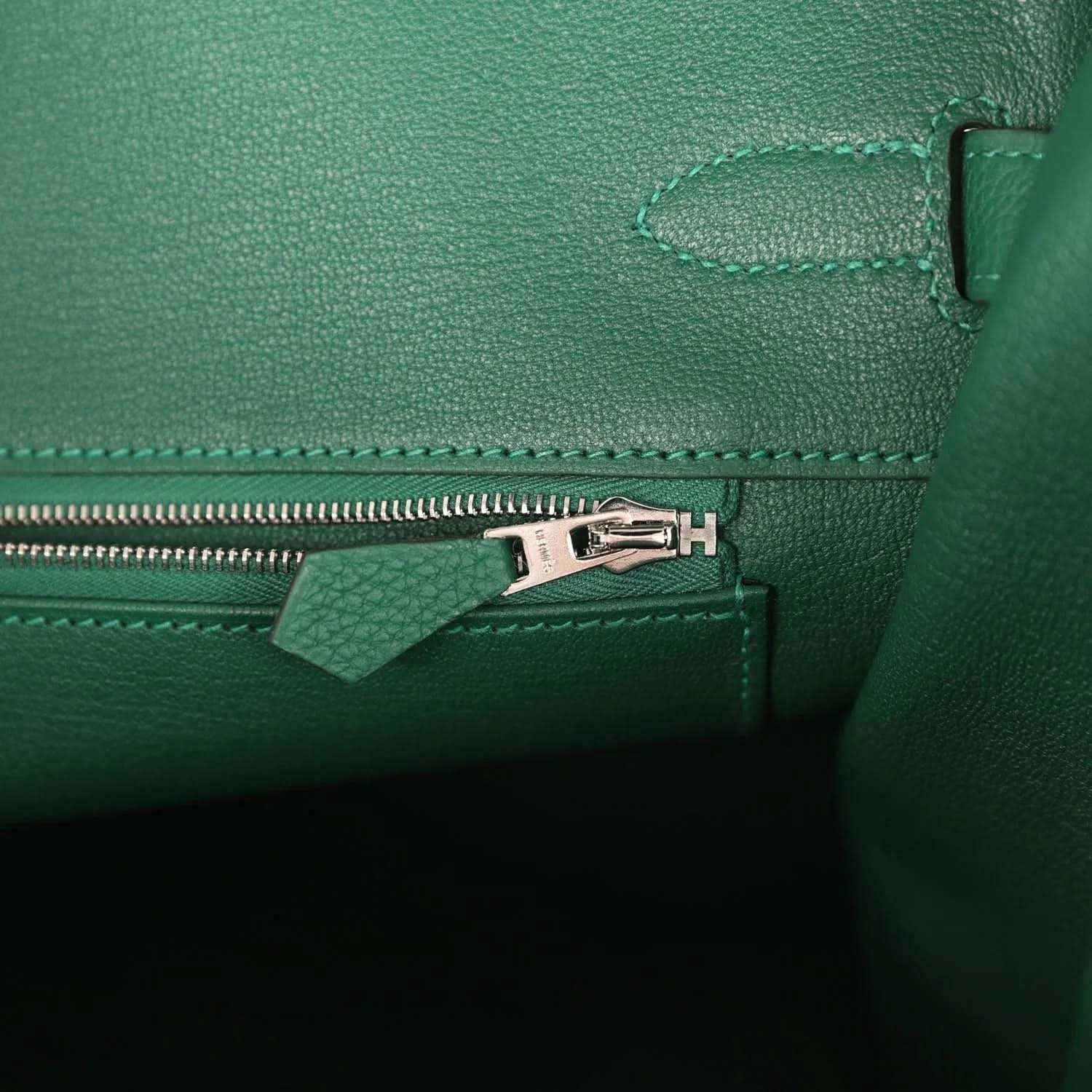 Green leather handbag interior detail with silver zipper pull and stitched seam trim