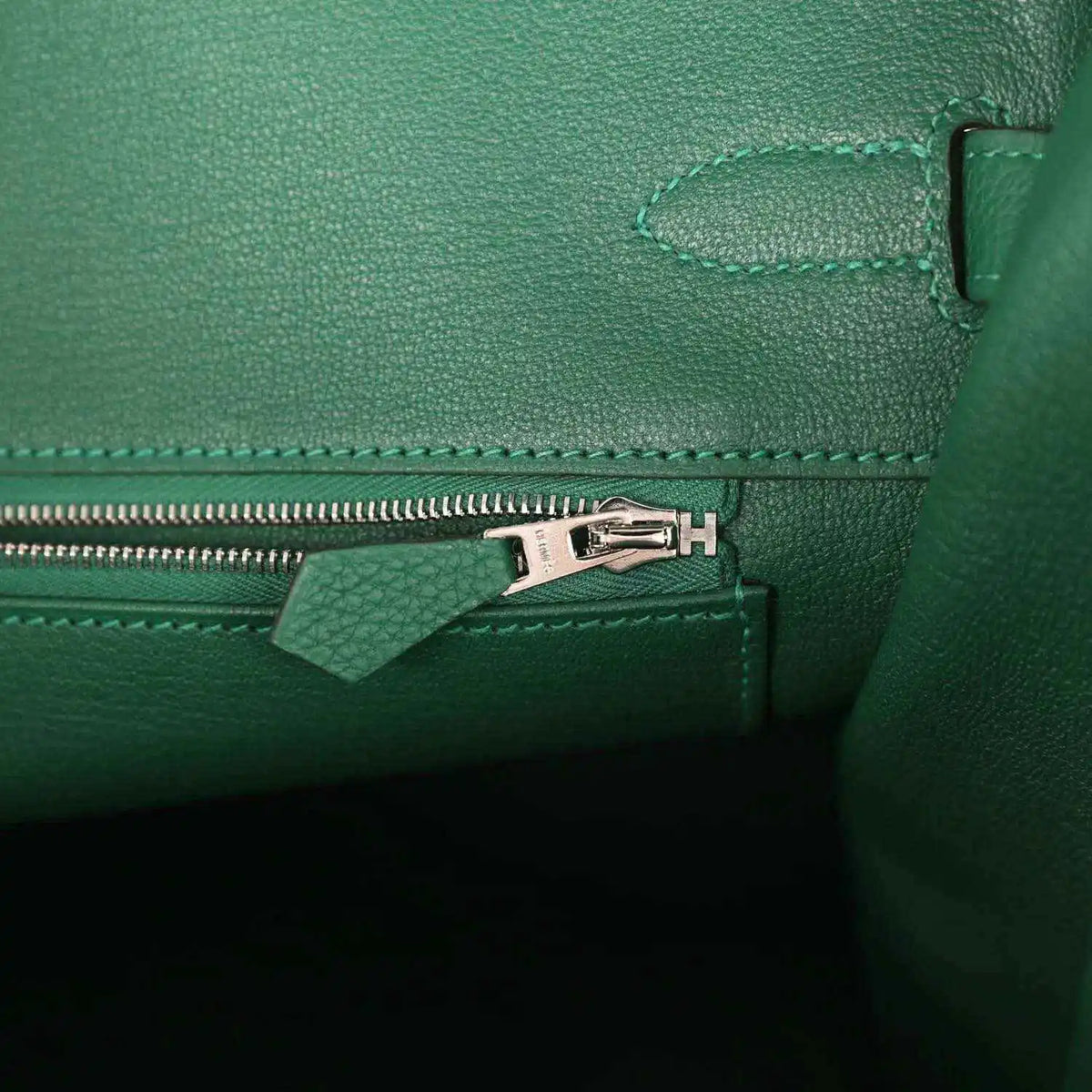 Green leather handbag interior detail with silver zipper pull and stitched seam trim