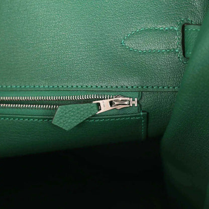 Green leather handbag interior detail with silver zipper pull and stitched seam trim