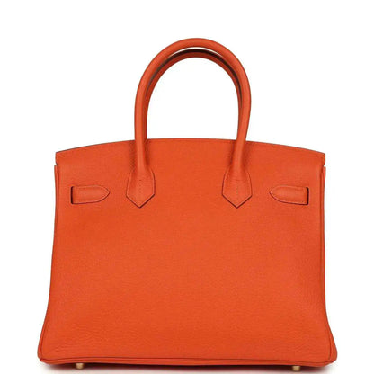 Orange leather handbag back view with two top handles and minimal front hardware.