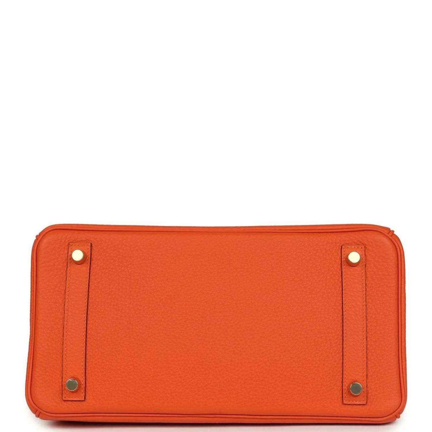 Orange leather handbag back panel with snap tabs and metal feet at base.