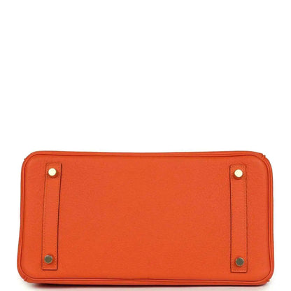 Orange leather handbag back panel with snap tabs and metal feet at base.