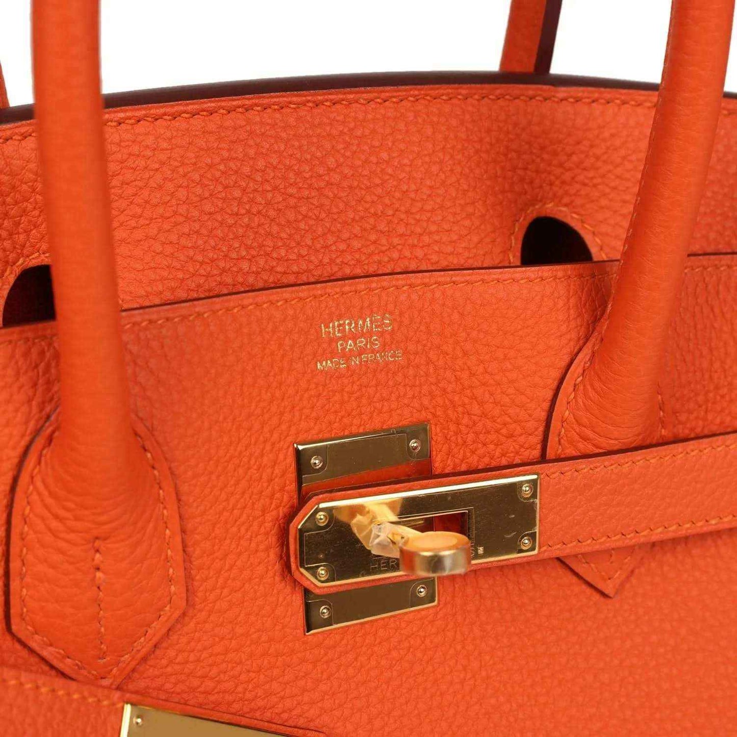 Orange leather handbag interior with embossed logo and gold-tone lock hardware.