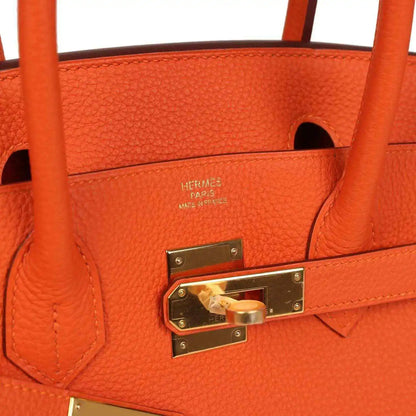 Orange leather handbag interior with embossed logo and gold-tone lock hardware.