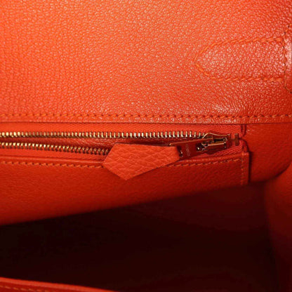 Orange leather handbag interior zipper with pull tab and stitched fabric trim.