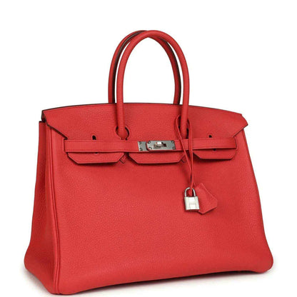 Red leather handbag with top handles, front flap detailing, and silver-tone clasp hardware