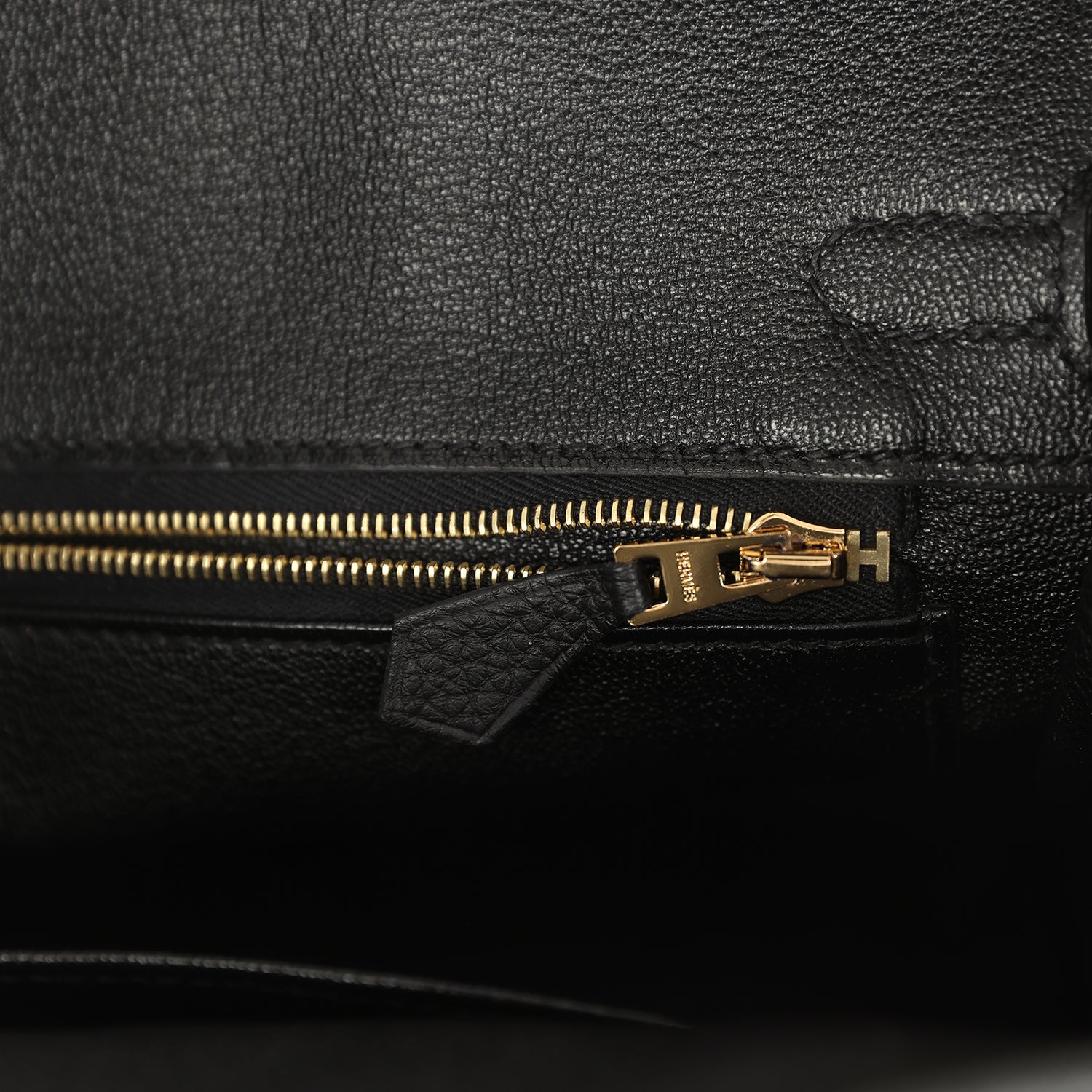 Black leather handbag zipper with gold-tone pull and leather tab