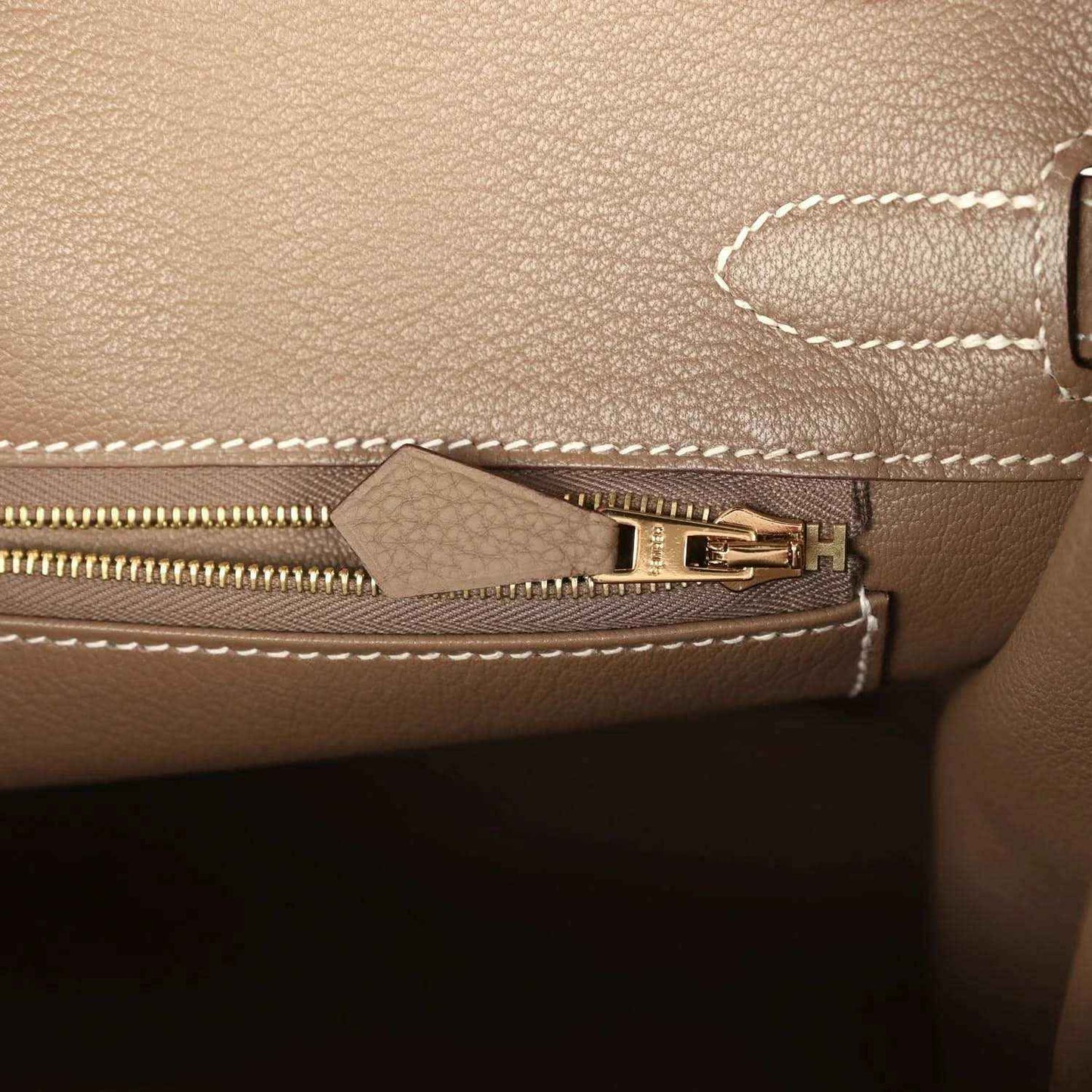 Taupe leather handbag close-up with brushed gold clasp, top handle and contrast stitching