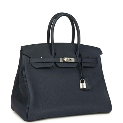 Navy leather handbag with front flap, top handles, and hanging padlock