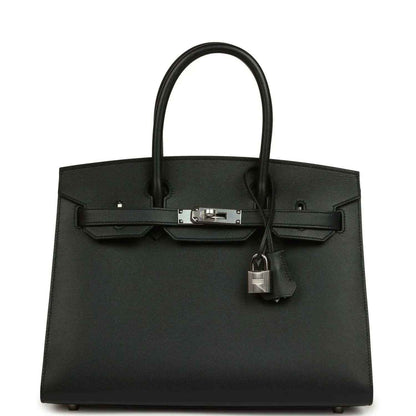 Black leather handbag with top handles, front clasp, and hanging lock charm