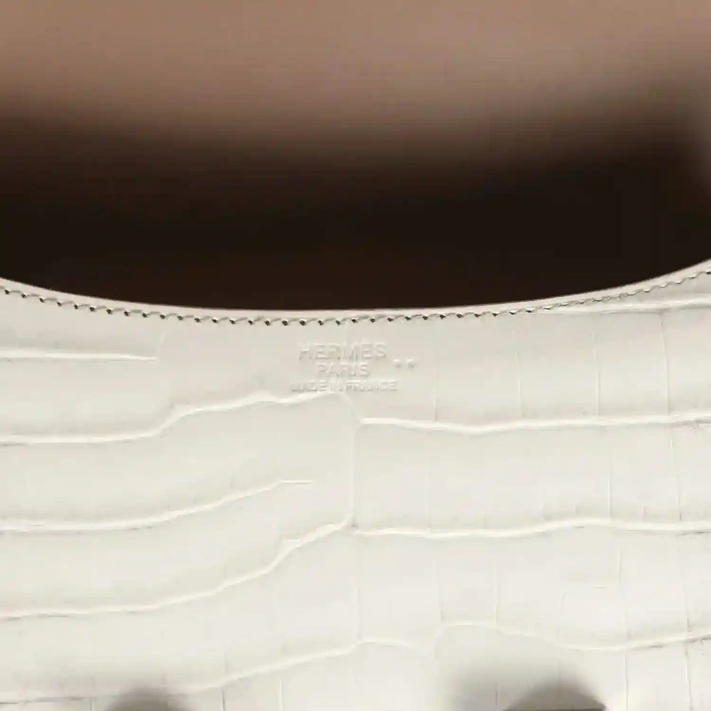 Close-up of light gray croc-embossed leather with stitched edge and small brand stamping
