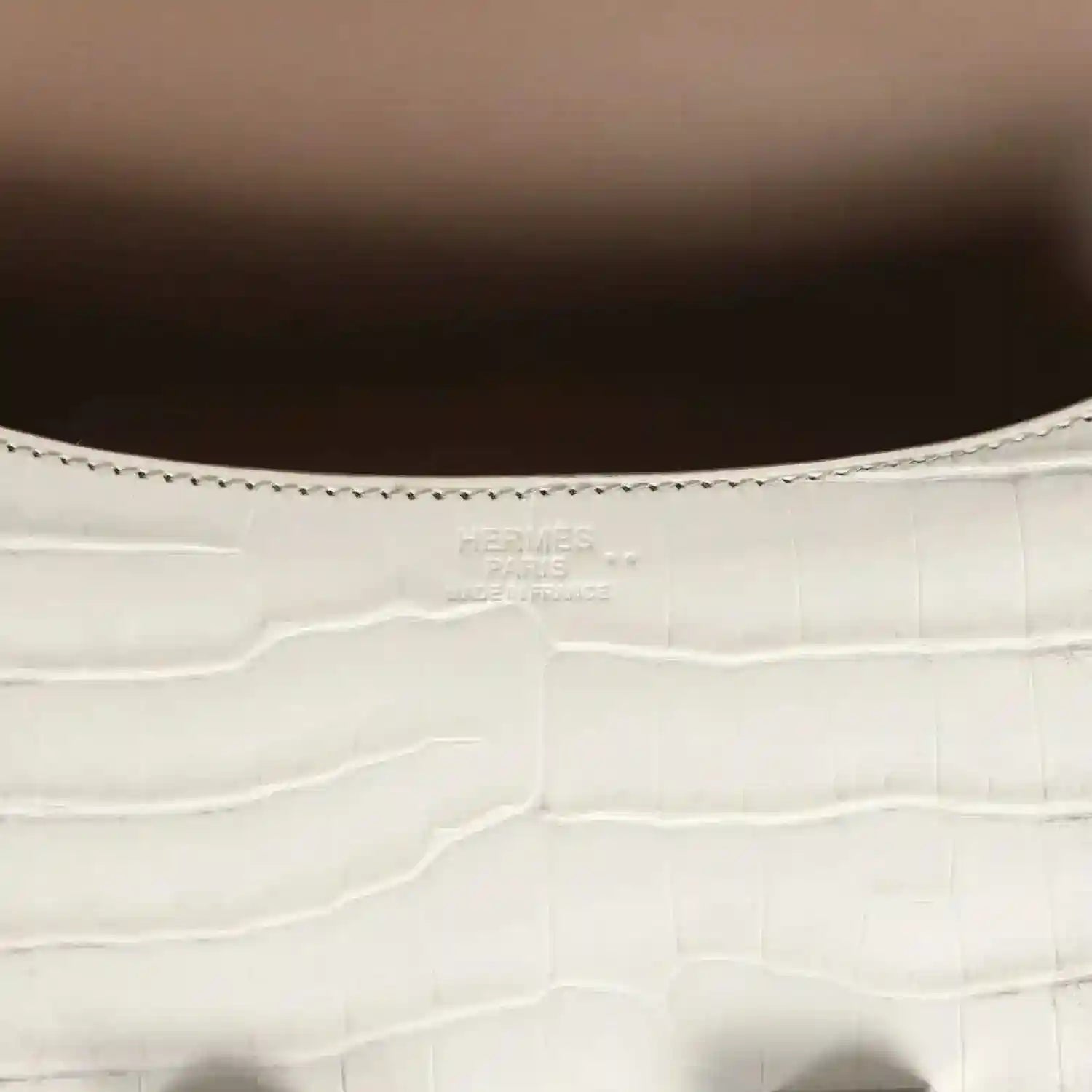 Close-up of light gray croc-embossed leather with stitched edge and small brand stamping