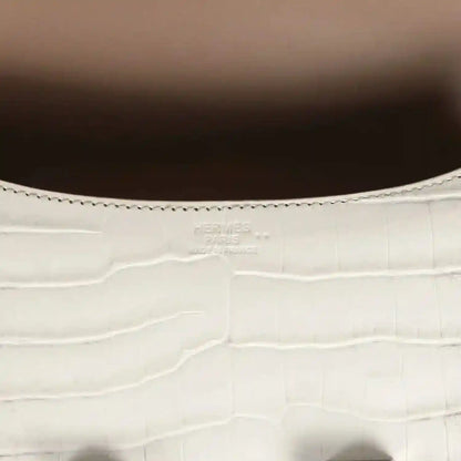 Close-up of light gray croc-embossed leather with stitched edge and small brand stamping