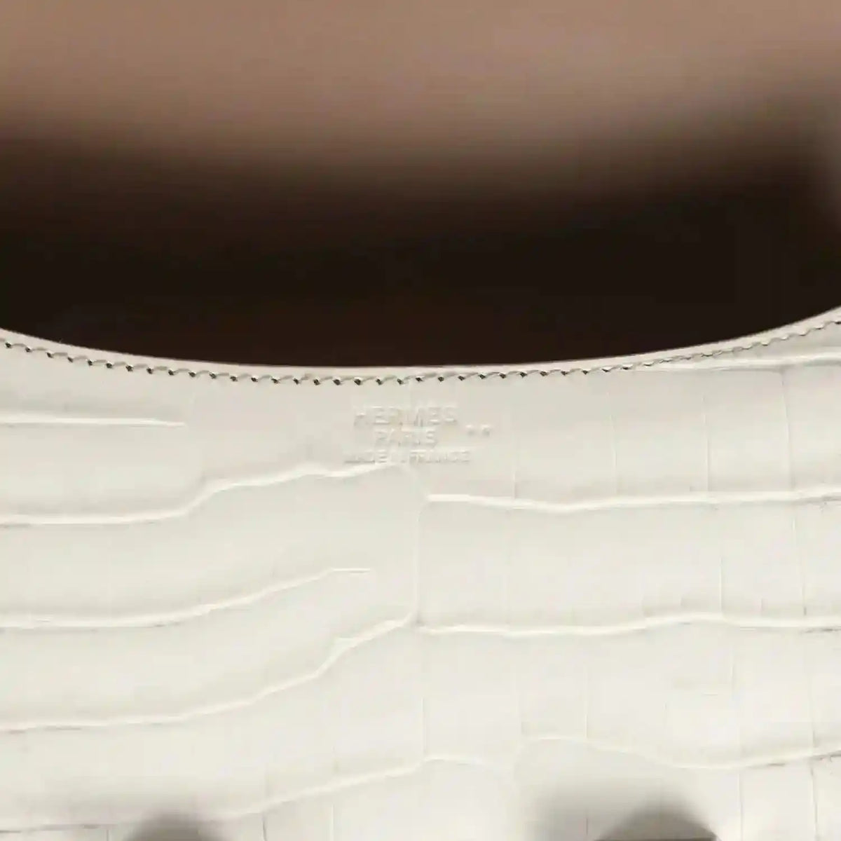 Close-up of light gray croc-embossed leather with stitched edge and small brand stamping