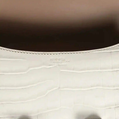Close-up of light gray croc-embossed leather with stitched edge and small brand stamping