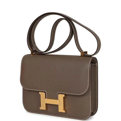 Taupe leather shoulder bag with gold H clasp, curved flap, and hanging shoulder straps